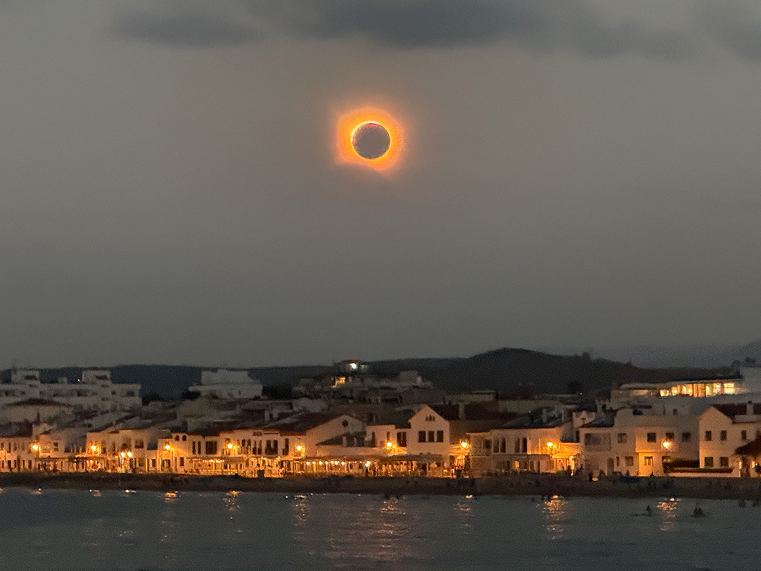 Solar eclipse over a Spanish town. The sea can be seen in the foreground. Solar eclipse over a Spanish town. The sea can be seen in the foreground.